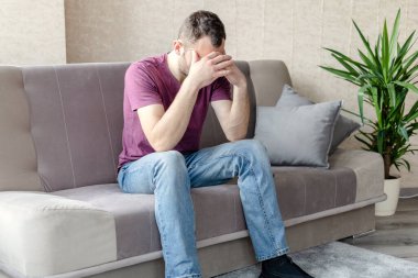 Genç üzgün adam, parlak bir odada, bir kanepede oturuyor.