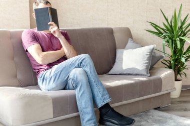 Sıkıntıdan patlayan genç adam kanepede otururken yüzünü kitapla örttü.