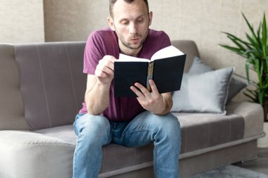 Genç adam bir kanepeye oturur ve faiziyle kitap okur.