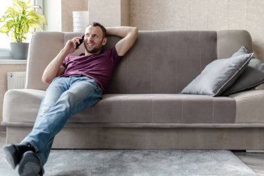 Genç ve mutlu bir adam kanepede oturup telefonda konuşuyor.