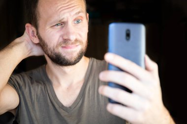 Şaşkın genç adam akıllı telefon ekranına bakıyor.