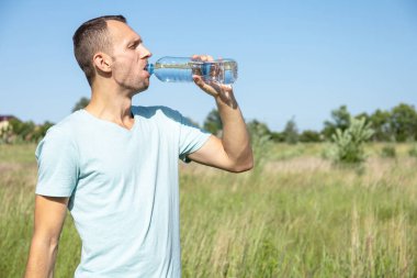 Genç adam doğadaki bir şişeden su içiyor.