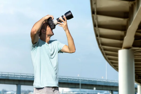 都会の建物を背景に大きなプロ仕様のカメラを持った若い男性写真家が — ストック写真