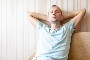 Adam evinde, kanepede gözleri kapalı, elleri başının arkasında dinleniyor.