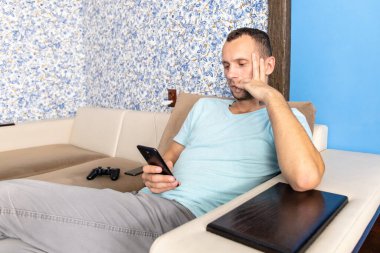 Genç adam bir kanepede otururken akıllı telefonun ekranına bakar.