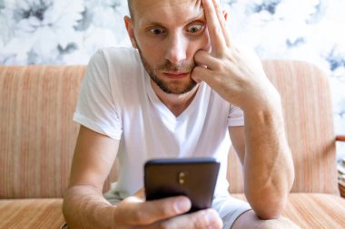 Şaşırmış ve korkmuş yüzlü genç bir adam akıllı telefonun ekranına bakar.