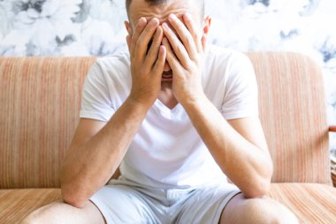 Üzgün adam elleriyle yüzünü örterek oturuyor.