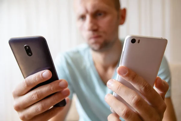 Elinde iki akıllı telefon olan bir adam onlara bakmayı seçiyor.