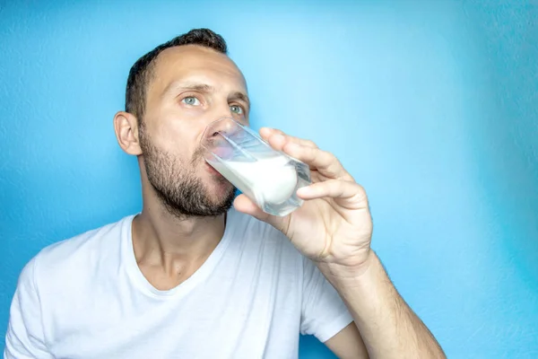 young man drinks milk from a glass cup, close-up
