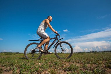 Güneşli bir günde bisikleti gökyüzüne dayanmış güzel bir genç adam.