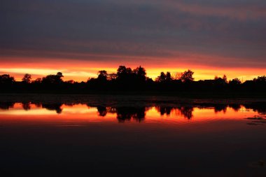 Gün batımı. Gökyüzünde büyük kara bulut ve parlak için dar bir şerit. Tüm gölde yansıyan.