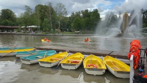 4 augusti 2020, Moskva, Ryssland, VDNH Park, gula och blå båtar står på sjön piren, Människor rider i parken på båtar, nära fontänen. — Stockvideo