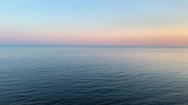 Pembe bir günbatımında, küçük dalgalarla sakin, rahatlatıcı bir deniz..
