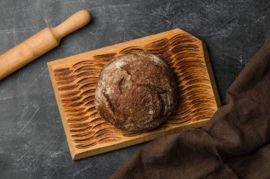 Koyu arka planda kırsal ekmek. Düz yatıyordu. El yapımı kesme tahtası.