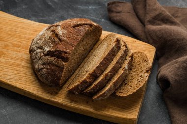 Koyu arka planda kırsal ekmek ve dilimler. El yapımı kesme tahtası.