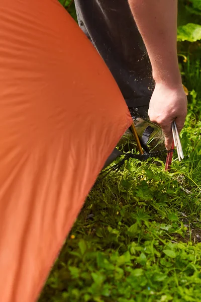 Close up man\'s hands sticks a peg into the ground while setting up a tent in the forest. tourists put up a tent in a camping