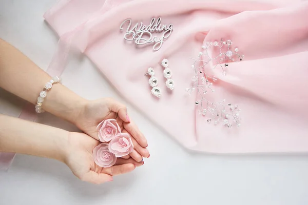 Mãos de noiva com flores de tecido decorativas em chiffon rosa no fundo de papel branco - visão superior — Fotografia de Stock
