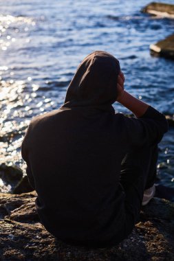 Bir kayanın üzerinde otururken ve okyanusu izlerken düşünen adam