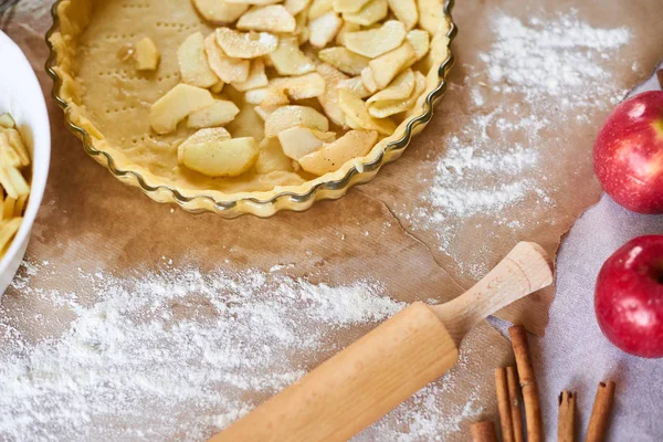 Vrouw voegt gesneden appels toe aan appeltaart. Vrouw hanteert een taartdeeg in een dienblad, op een keukentafel, omringd door pompoentaart ingrediënten. Traditionele taarten bakken — Stockfoto