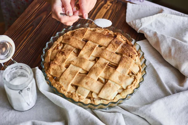 Mujer rociando pastel de manzana recién hecho con azúcar en polvo en la mesa — Foto de Stock