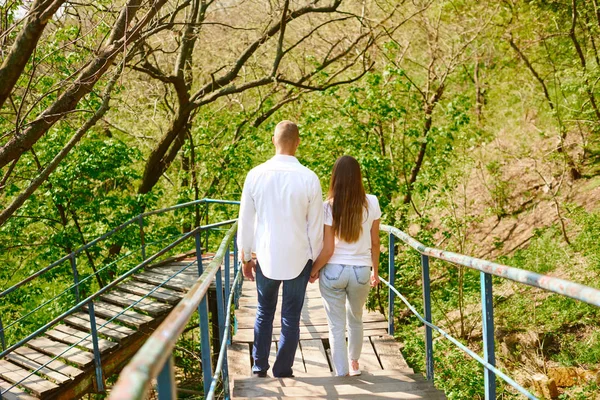 Pareja joven enamorada, chica con una camiseta blanca y un chico con una camisa blanca bajan las escaleras tomados de la mano — Foto de Stock