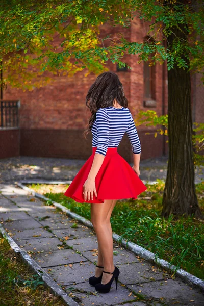 年轻的黑发女子，笑着在公园里纺纱。 穿红裙的女孩在户外跳舞 — 图库照片