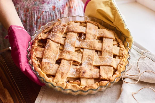 A woman holding a fresh baked apple tart . Woman putting delicious american pie on table. the housewife in the kitchen mittens delivers the apple pie to the table. — Stock Photo, Image