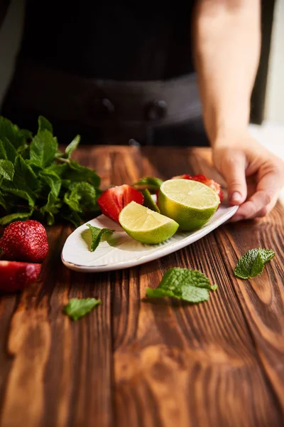 Lime strawberry mint ingredients for making lemonade on white plate on wooden table — Stock Photo, Image