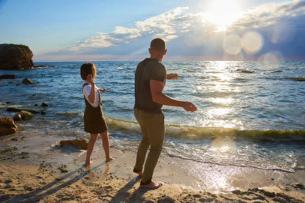 Pareja cariñosa al amanecer playa lanzando una piedra en el mar. hermoso romántico amor fondo —  Fotos de Stock
