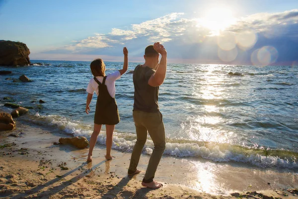 Feliz pareja amorosa conocer el amanecer y jugar en la playa en la orilla del mar. resplandor del sol en el marco —  Fotos de Stock