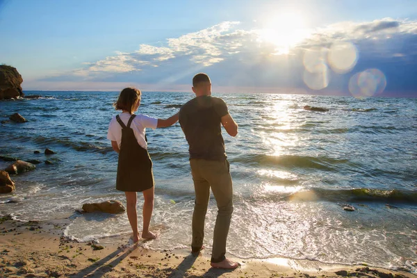 Pareja cariñosa al amanecer playa lanzando una piedra en el mar. hermoso romántico amor fondo — Foto de Stock