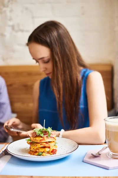 Красивая молодая женщина с мобильным телефоном ест вкусные блины в кафе — стоковое фото