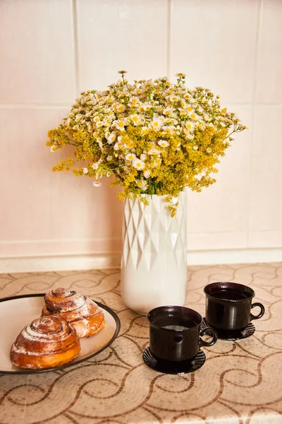 テーブルの上にスタイリッシュな白い花瓶にハーブの花束。コーヒーとシナモンロールを2杯ホームコンフォートコンセプト — ストック写真