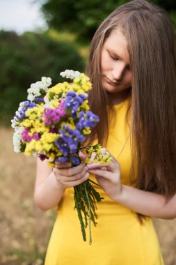 Parkta duran uzun saçlı sarışın kız. Elinde çiçekler tutuyordu. Alanlardan mevcut