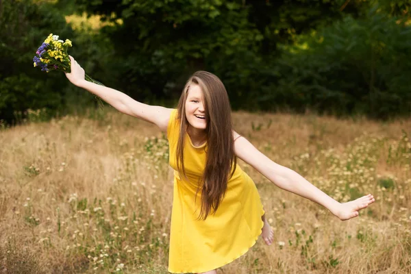 一头金发的女孩单腿站在公园里笑着。她手里拿着花。来自外地的 — 图库照片