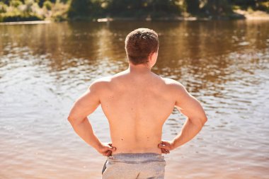 çıplak gövdeile kaslı bir adam sıcak bir günde bir nehir veya gölün kıyısında duruyor