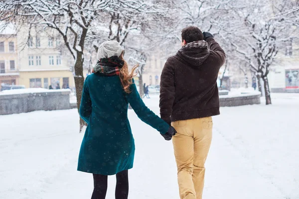 Jovem casal amoroso vestido com lenços xadrez andar, correr e rir da cidade velha no inverno. homem e mulher em estilo casual estão no parque de neve — Fotografia de Stock