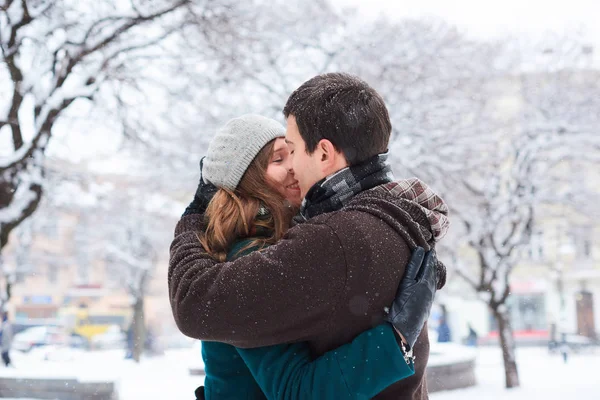 Pareja joven y cariñosa vestida con bufandas a cuadros camina por la ciudad vieja en invierno. Abrazos y besos — Foto de Stock