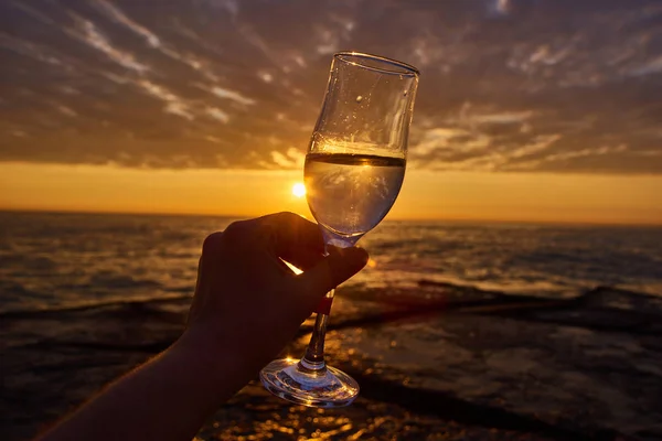 Morning energy. hand holding glass of white wine and with sea and beautiful sunrise at background, close-up. Holiday, day off morning relaxed mood concept — Stock Photo, Image