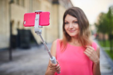 Genç kız, şehir caddesinde gezerken cep telefonuyla selfie çekiyor.