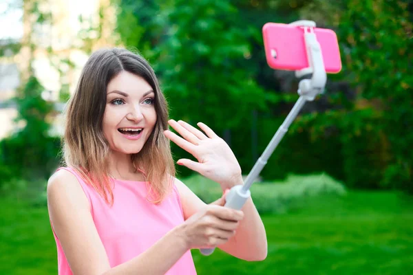 Genç bir kadın selfie çekiyor ve arkadaşına gülümseyerek video mesajı gönderiyor. Pembe elbiseli kız cep telefonunu tut ve yüz ifadesiyle oyna.