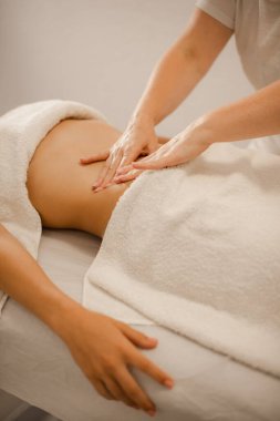 Masajcının elleri masaj salonundaki müşterinin midesine masaj yapıyor.