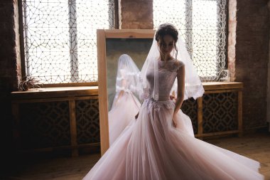 Gelin sabah aynanın yanında toplanıyor. Gelin sabah toplanıyor. Şık pembe gelinlik. Gelin aynaya yakın bir elbise içinde dönüyor..