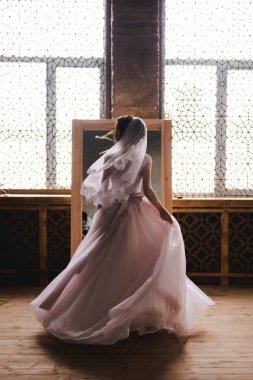 Gelin sabah aynanın yanında toplanıyor. Gelin sabah toplanıyor. Şık pembe gelinlik. Gelin aynaya yakın bir elbise içinde dönüyor..