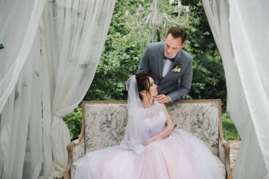 Düğün. Gelin ve damat bahçede bir çardak güzel bir kanepede oturuyorlar. Pembe elbiseli gelin, gri takım elbiseli damat. Beyaz çadır. Gelin ve damat ormanda yürüyorlar..