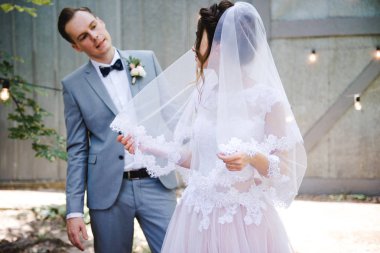 Düğün. Güzel bir gelin ve damadın portresi. Gelin ve damat ampuller ve metal kapılar bir çelenk fon karşı bahçede yürümek. Yeşil ve çiçek buketi.