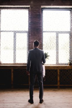 Damat gri takım elbiseli gelini bekliyor. Damat buket tutan ve gelin bekliyor. Düğün günü. Damat büyük bir pencerenin yanında duruyor.
