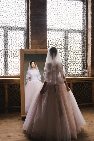 La novia se reúne por la mañana cerca del espejo. La novia se reunirá por la mañana. Elegante vestido de novia rosa. La novia está girando en un vestido cerca del espejo . — Foto de Stock