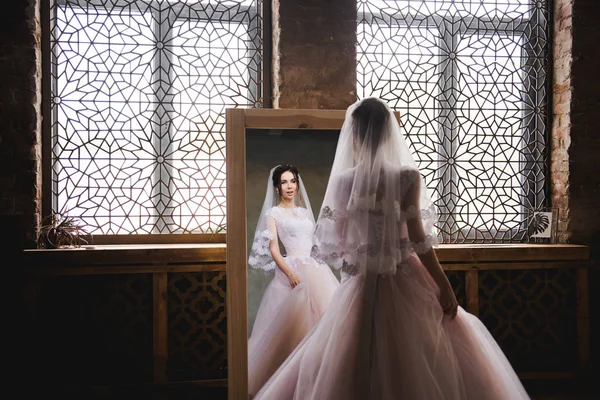 Die Braut versammelt sich am Morgen vor dem Spiegel. die Braut versammelt sich am Morgen. stilvolles rosa Hochzeitskleid. die Braut dreht sich in einem Kleid neben dem Spiegel. — Stockfoto