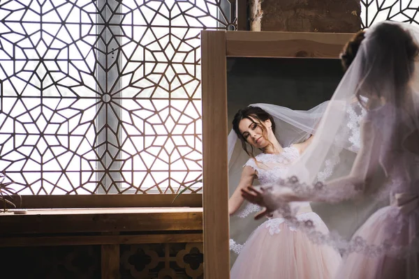 La novia se reúne por la mañana cerca del espejo. La novia se reunirá por la mañana. Elegante vestido de novia rosa. La novia está girando en un vestido cerca del espejo . — Foto de Stock